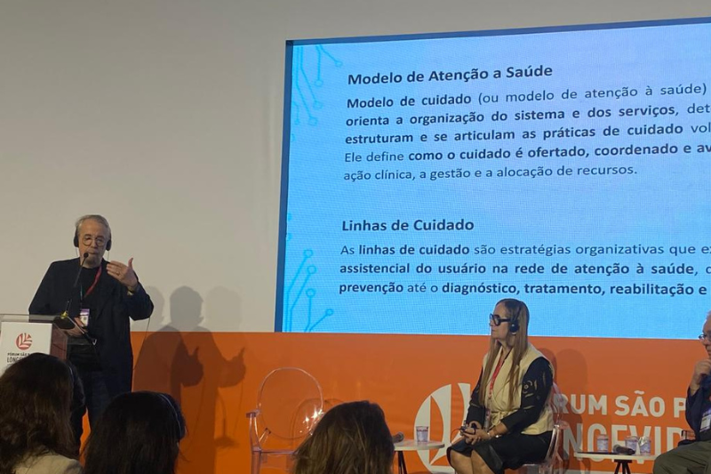 Ex-diretor da Agência Nacional de Saúde Suplementar, João Luís Barroca, fala em cima de um palco na frente de uma apresentação de slides