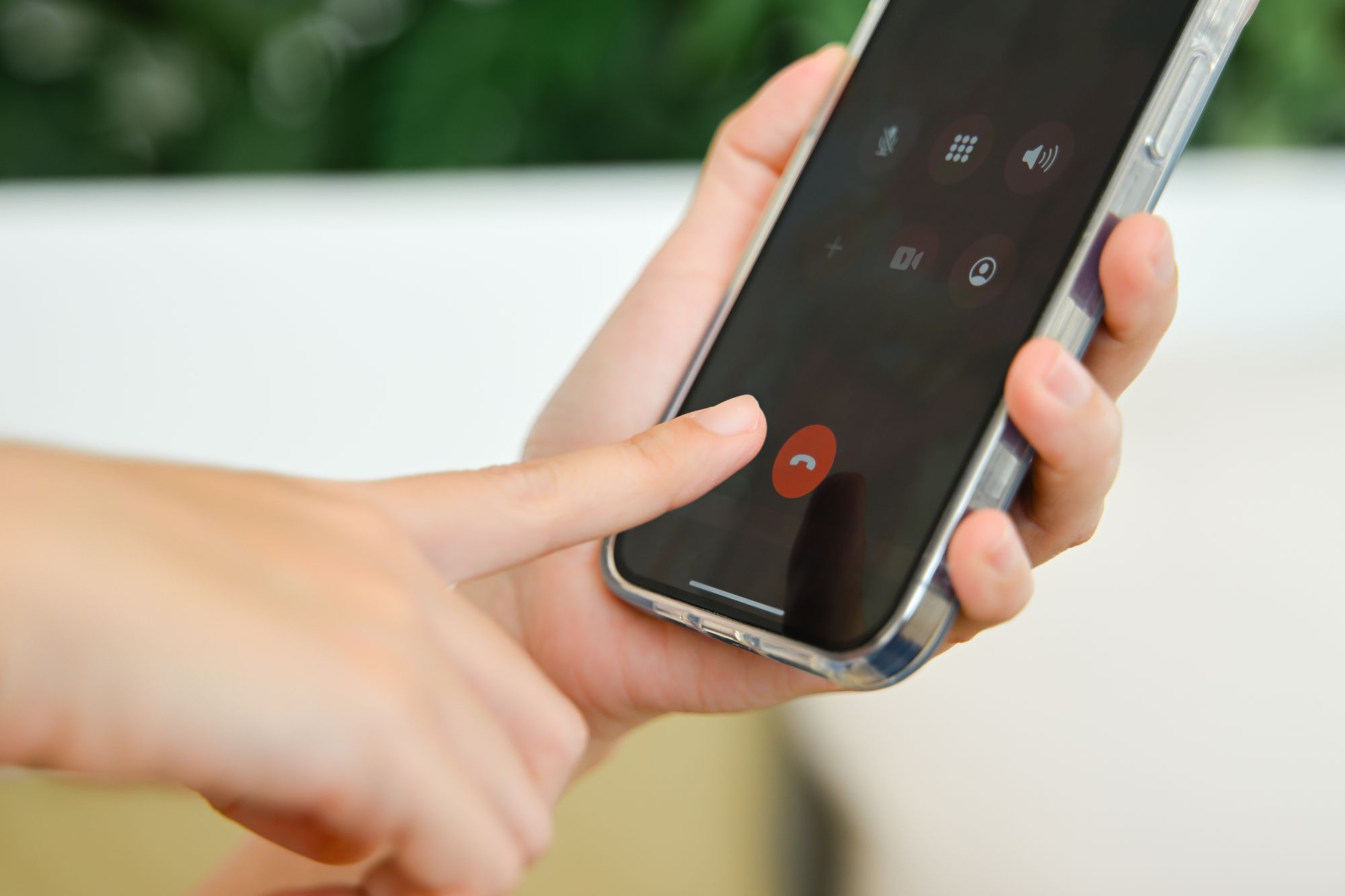 mão segurando smatphone e com dedo prestes a apertar o botão que desliga a chamada de voz