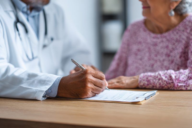 Uma idosa em frente a um médico enquanto ele prescreve uma receita