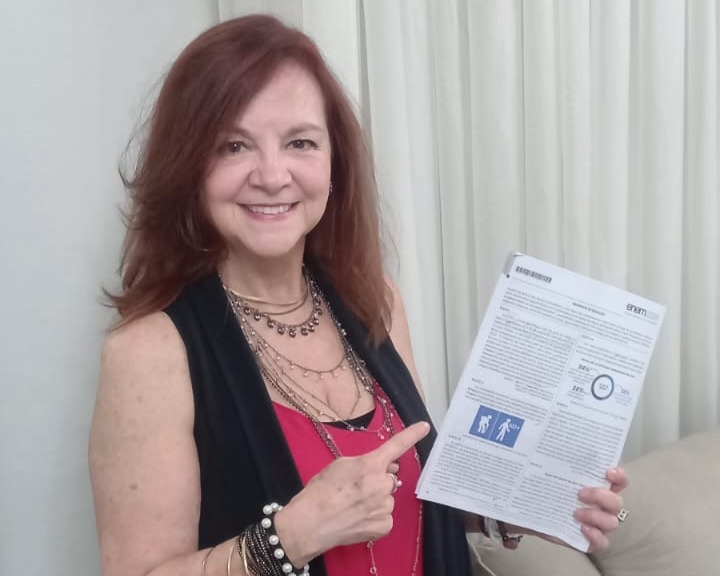 Mulher 50+ com cabelos vermelhos sorri enquanto segura prova do Enem 2025 nas mãos