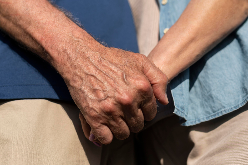 Um casal de senhor e senhora dando as mãos, foco da foto é nas mãos do casal