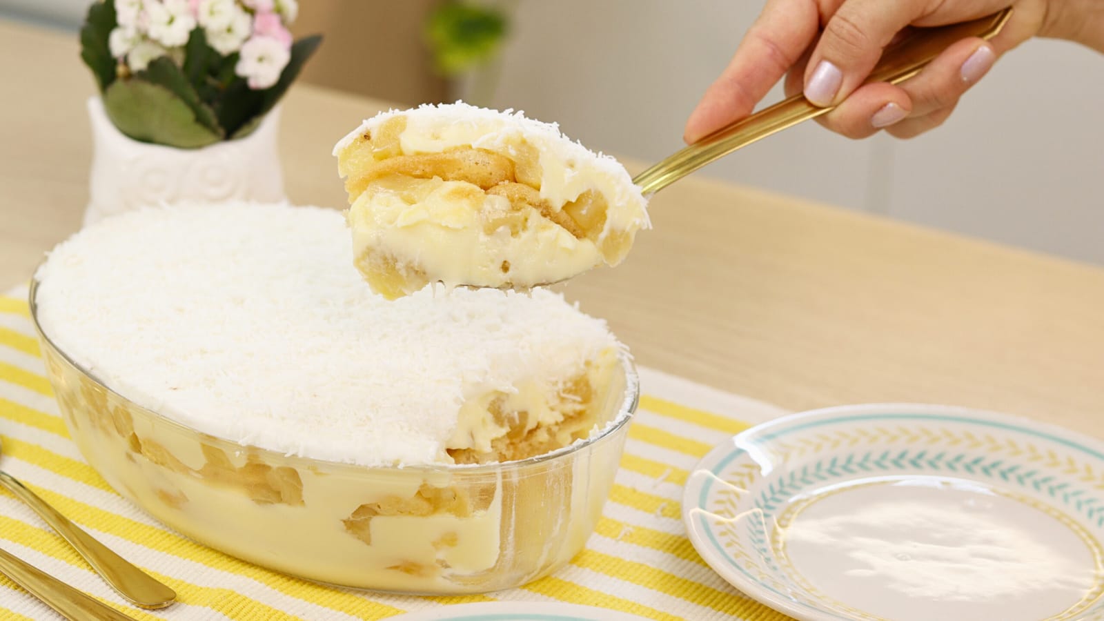 Pavê de abacaxi em cores brancas e amarelas leves, uma pessoa retira um pedaço do doce