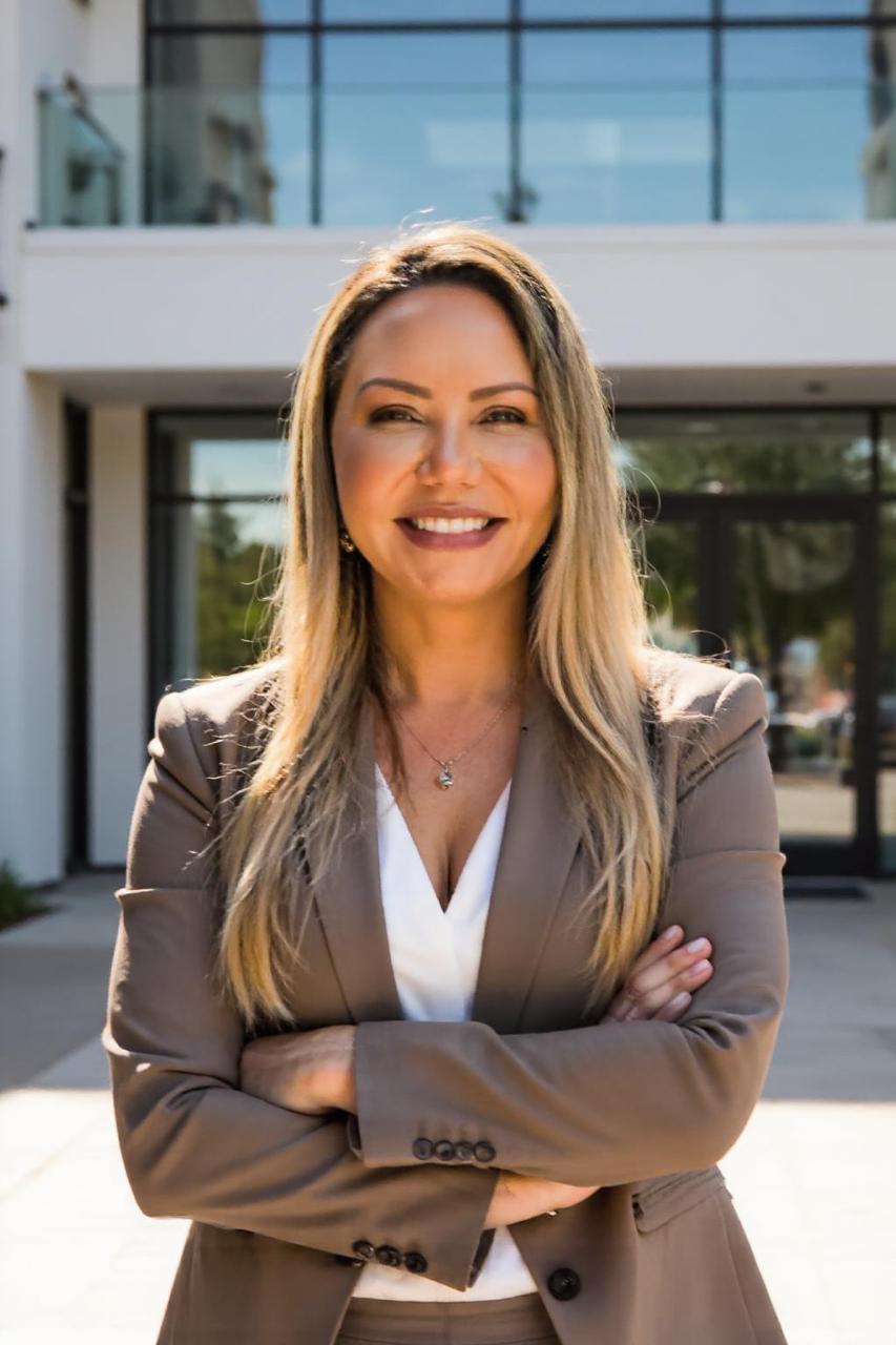 Siglia Azevedo, advogada, branca, loira, de cabeços longos, de terno cinza e camisa branca