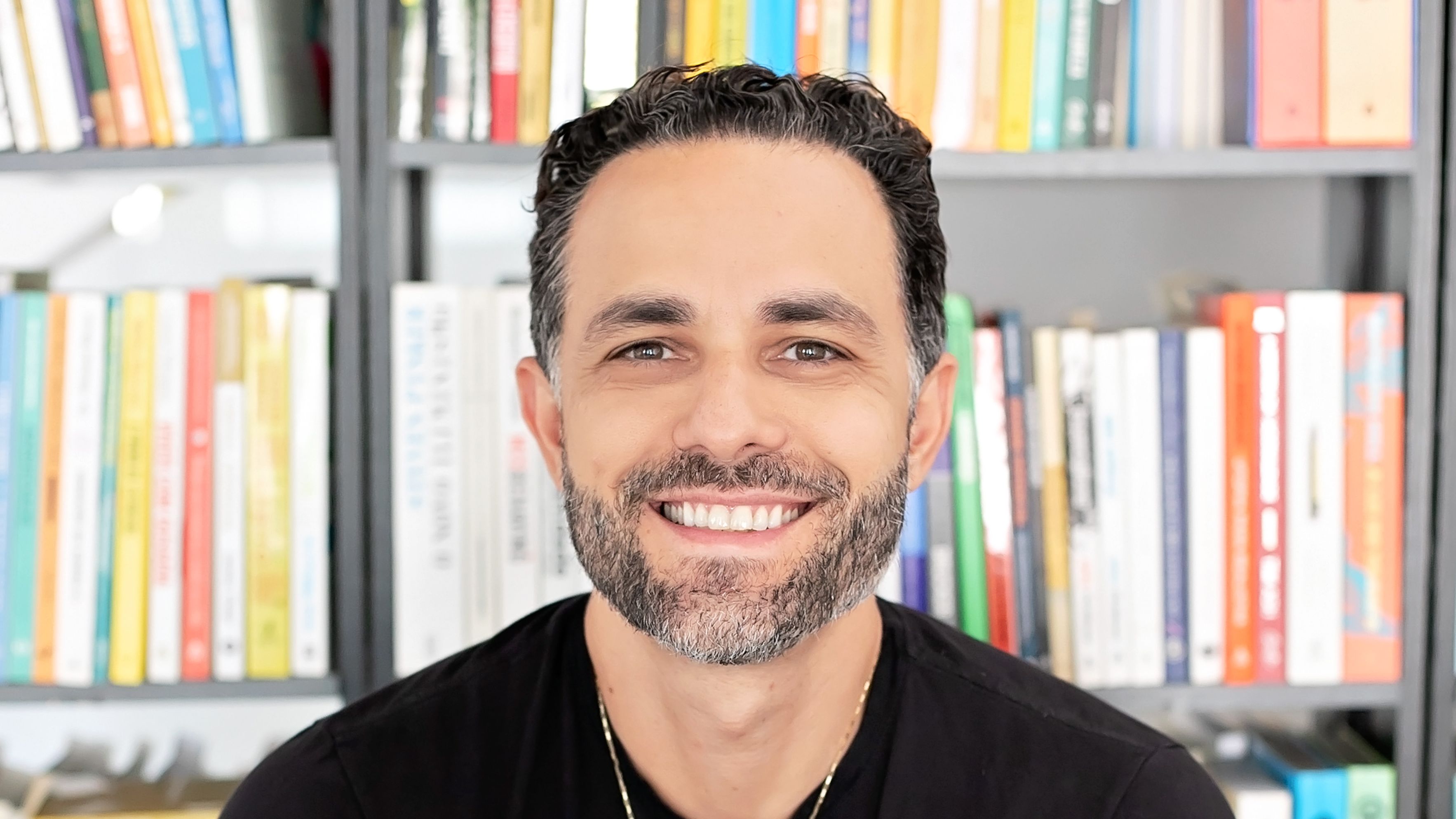 Thiago Godoy, educador financeiro, de camisa preta, com livros ao fundo
