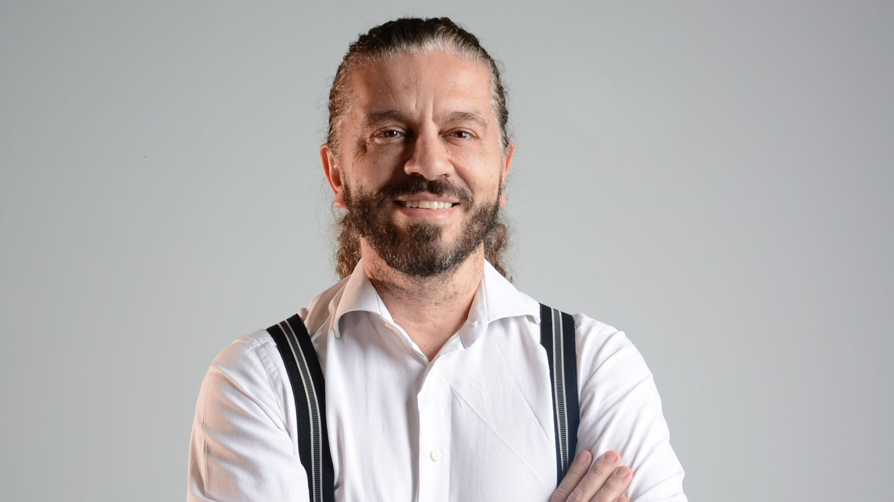 professor Alexandre Bertoncello, homem branco, de cabelos compridos e barba, veste blusa branca e suspensórios