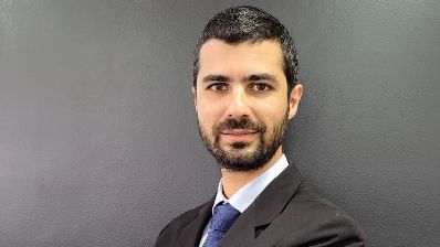 Lucas Sharau, homem branco de barba, veste terno cinza e gravata azul