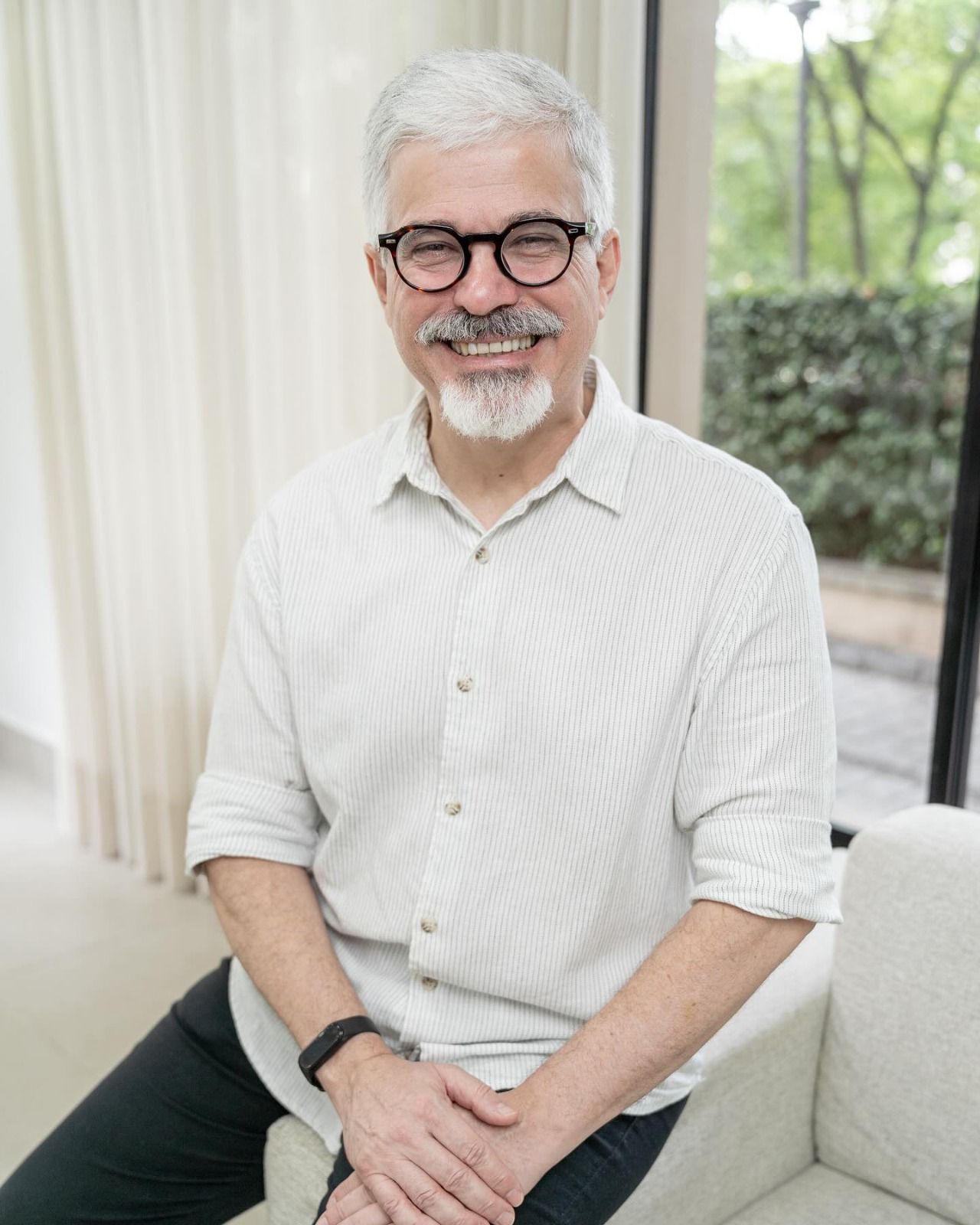 Edson Moraes, de cabelo e barba brancos, sentado em uma poltrona sorrindo para a câmera