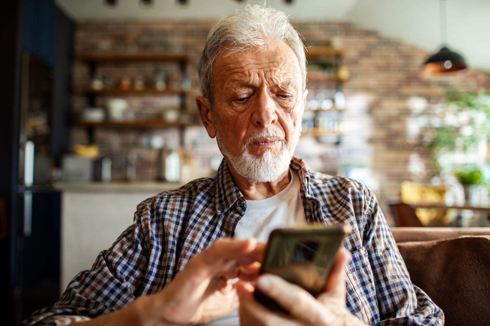 Homem idoso, de barba e cabelo brancos, usando um celular