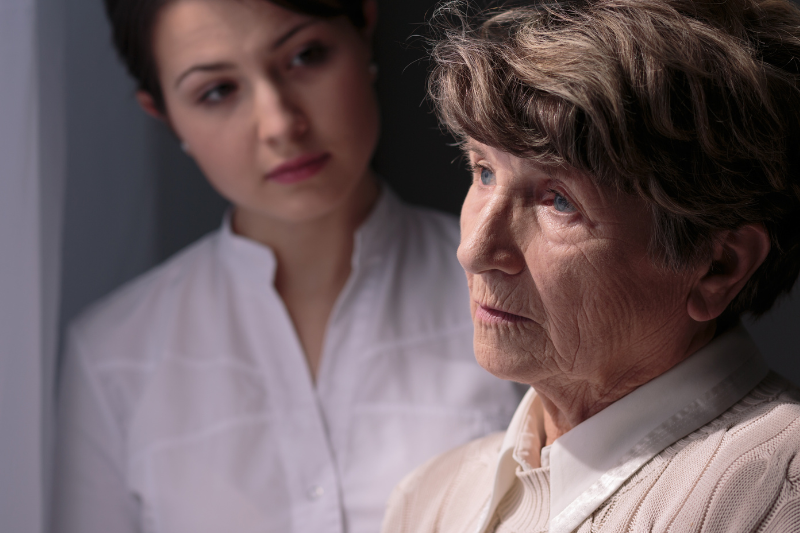 Mulher idosa com alzheimer olha para o horizonte, enquanto uma mulher mais nova a encara