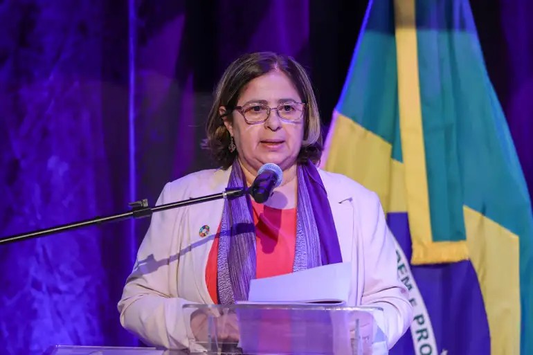 Ex ministra discursa com  foto da Bandeira Nacional ao fundo