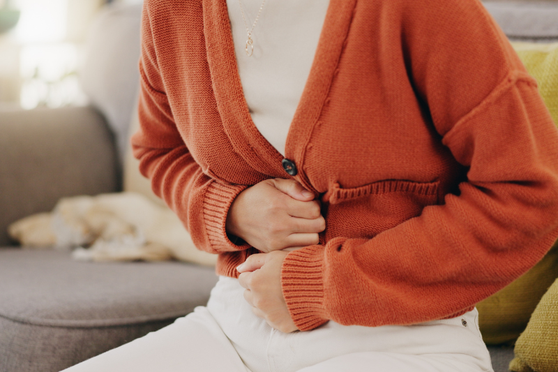 mulher sentada no sofá abraça a barriga em sinal de cólicas de menstruação ou endometriose