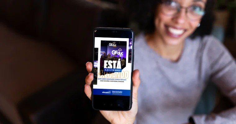 Jovem sorrindo mostra tela do aplicativo do GEduc no celular