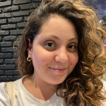 Julia é uma mulher branca que sorri para a foto. tem cabelos enrolados em tons escuros e loiros