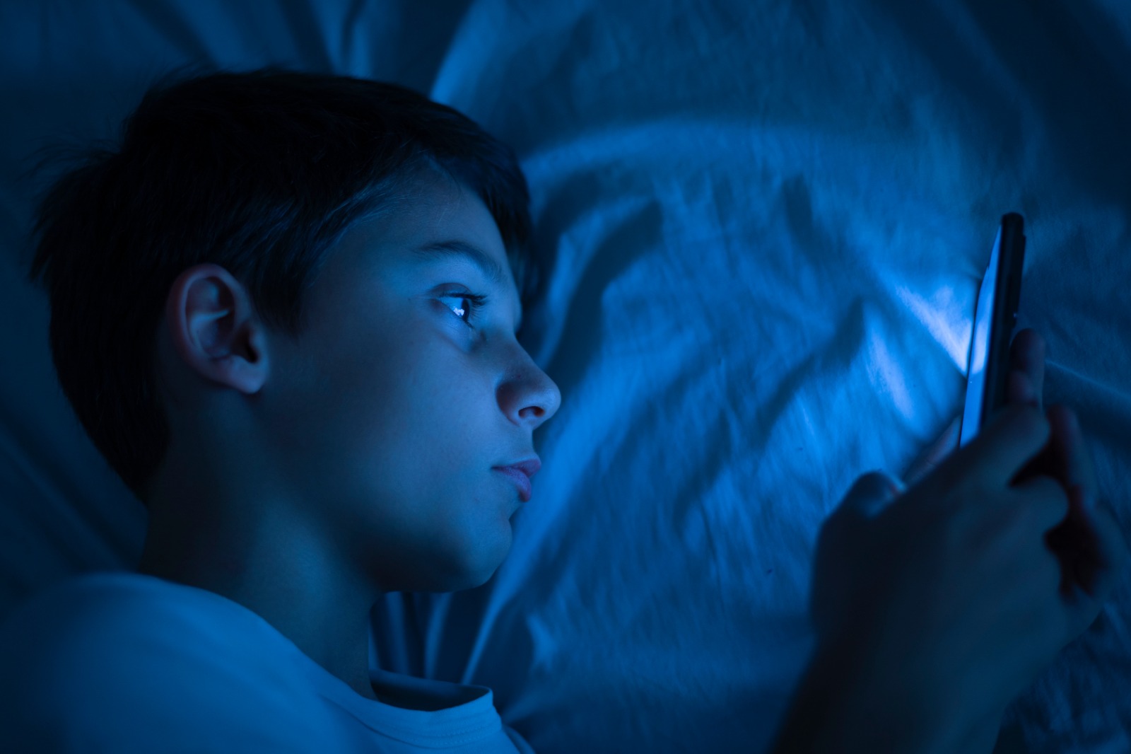 Um menino usando o celular a noite, deitado na cama