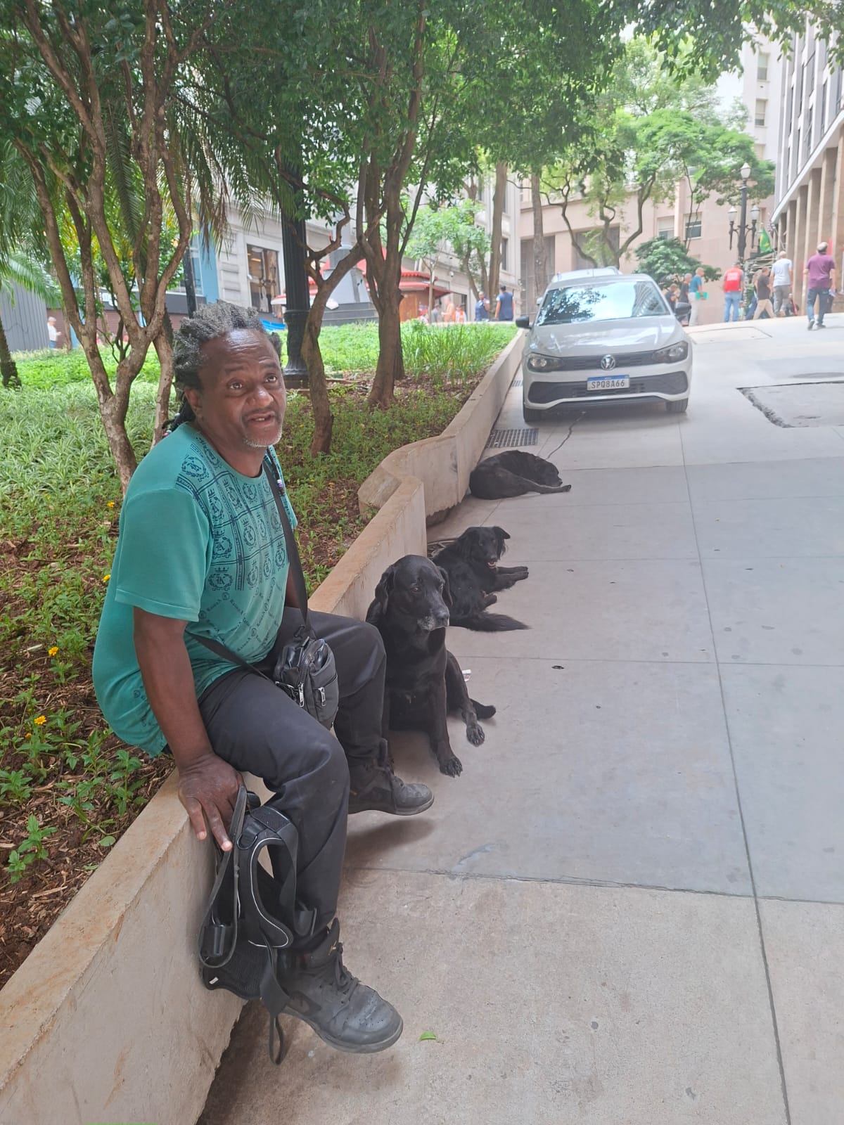 Morador de rua sentado em mureta ao lado de seus cães 