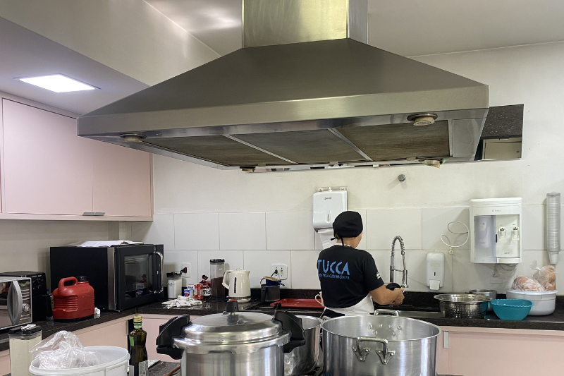 cozinha do TUCCA, com paredes rosas. Há uma colaboradora cozinhando ao fundo