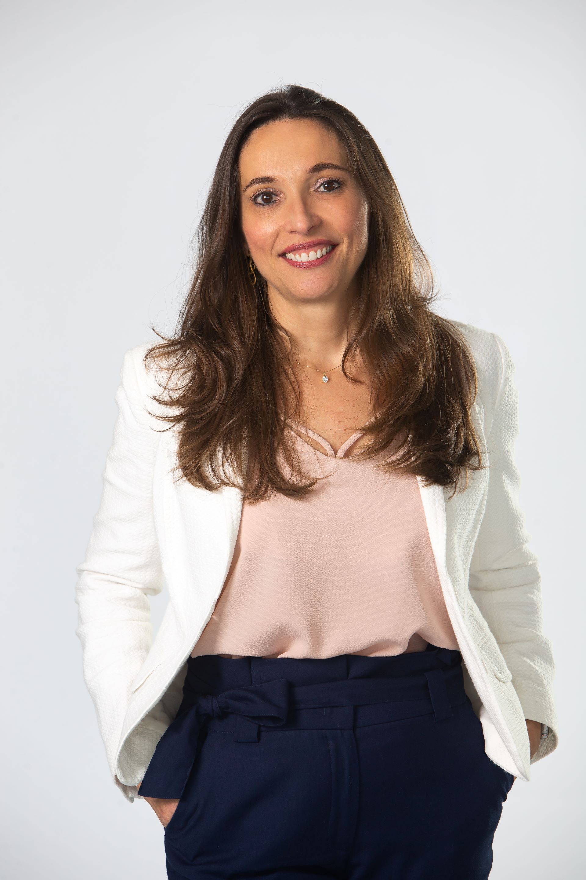 A professora Ana Paula Serra, de cabelos comprido à altura do peito, sorri usando um blazer claro e blusa rosa