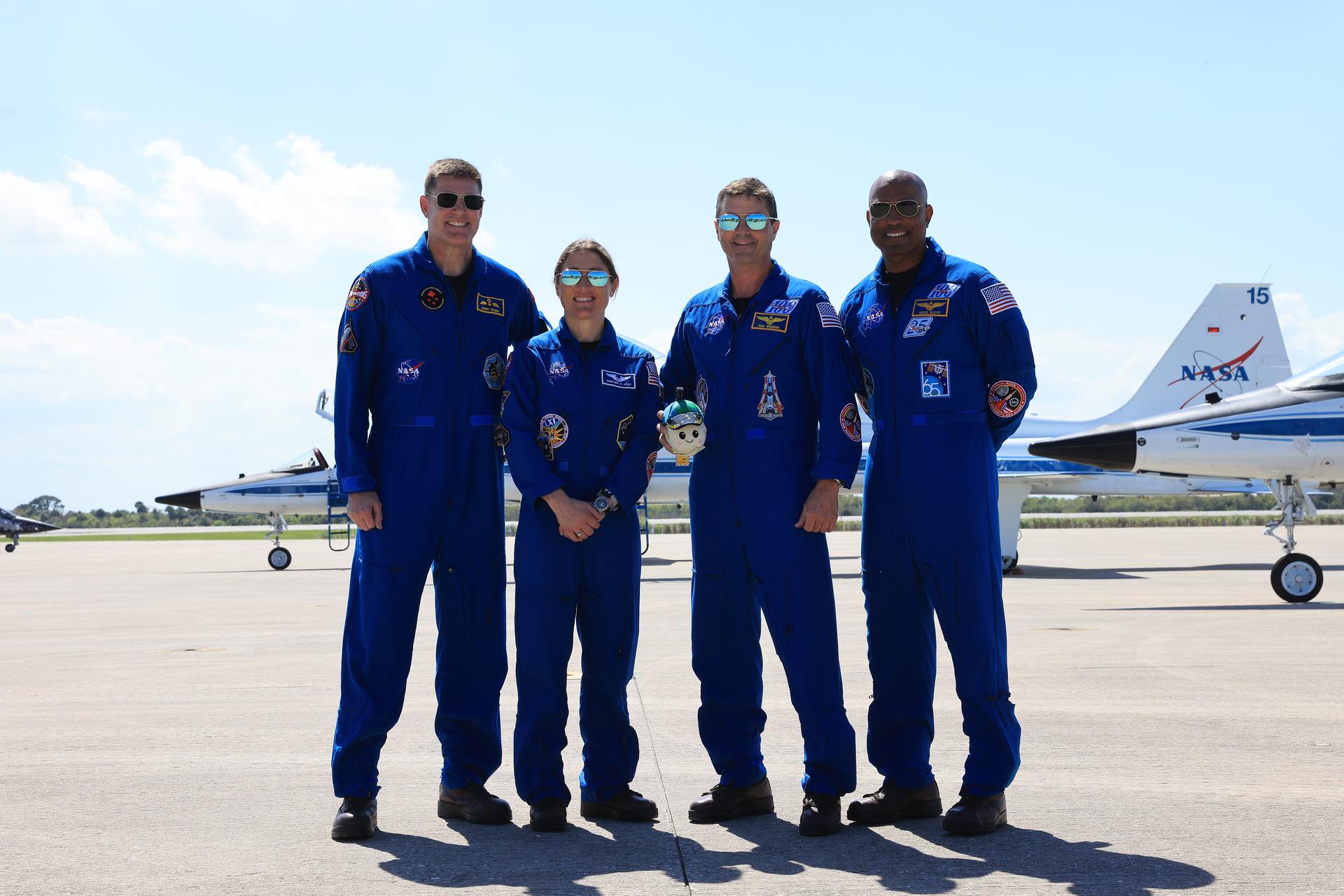 Os astronautas de pé, em solo, usando macações azuis: Jeremy Hansen, Christina Koch, Reid Wiseman e Victor Glover