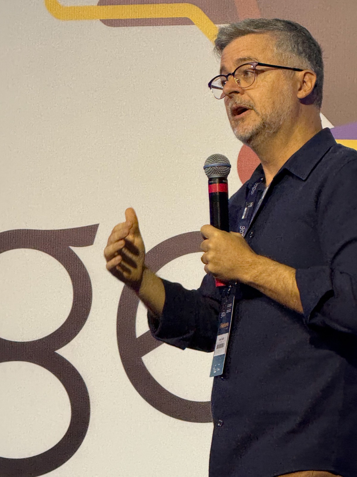 Foto de Daniel Barros falando ao microfone em um palco