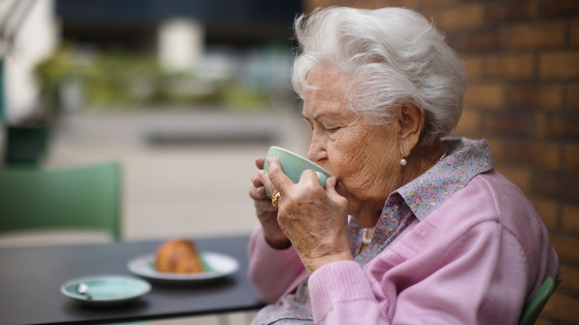 Senhora idosa feliz desfrutando de uma xícara de café e do café da manhã em um café na cidade