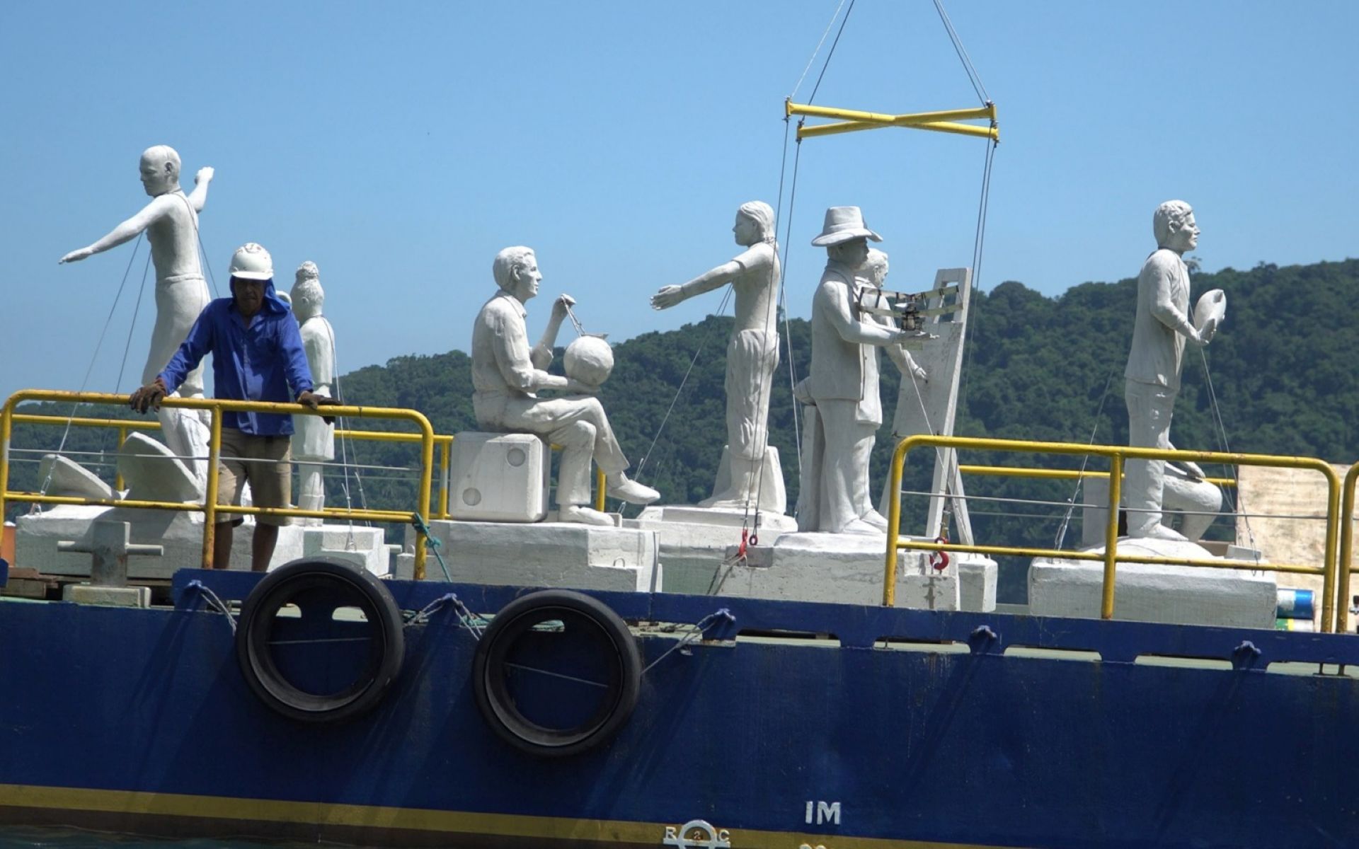 Uma série de esculturas sendo transportadas em cima de uma embarcação