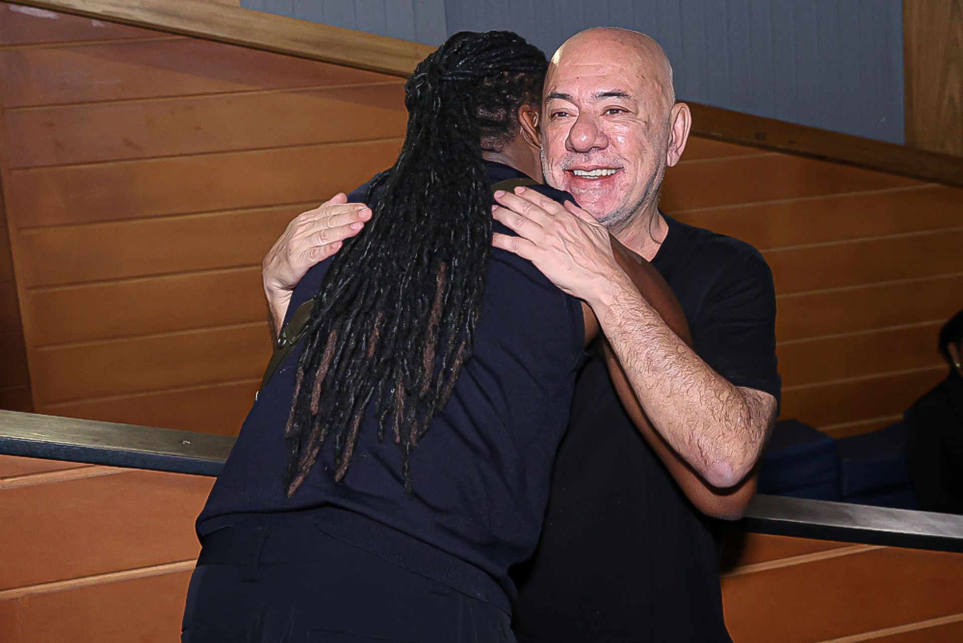 Claudio Torres aparece sorrindo, sendo abraçado por Lázaro Ramos