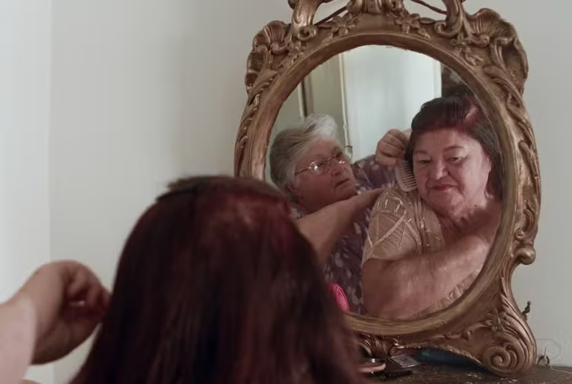 Uma mulher está ajudando a outra a se arrumar diante do espelho