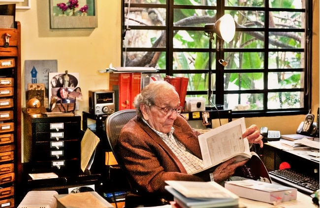 Alberto Dines está em seu escritório, olhando um livro