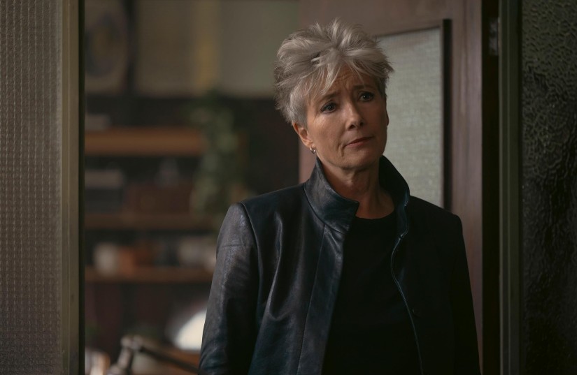 A atriz Emma Thompson em cena de filme, aparece em pé usando roupas acinzentadas