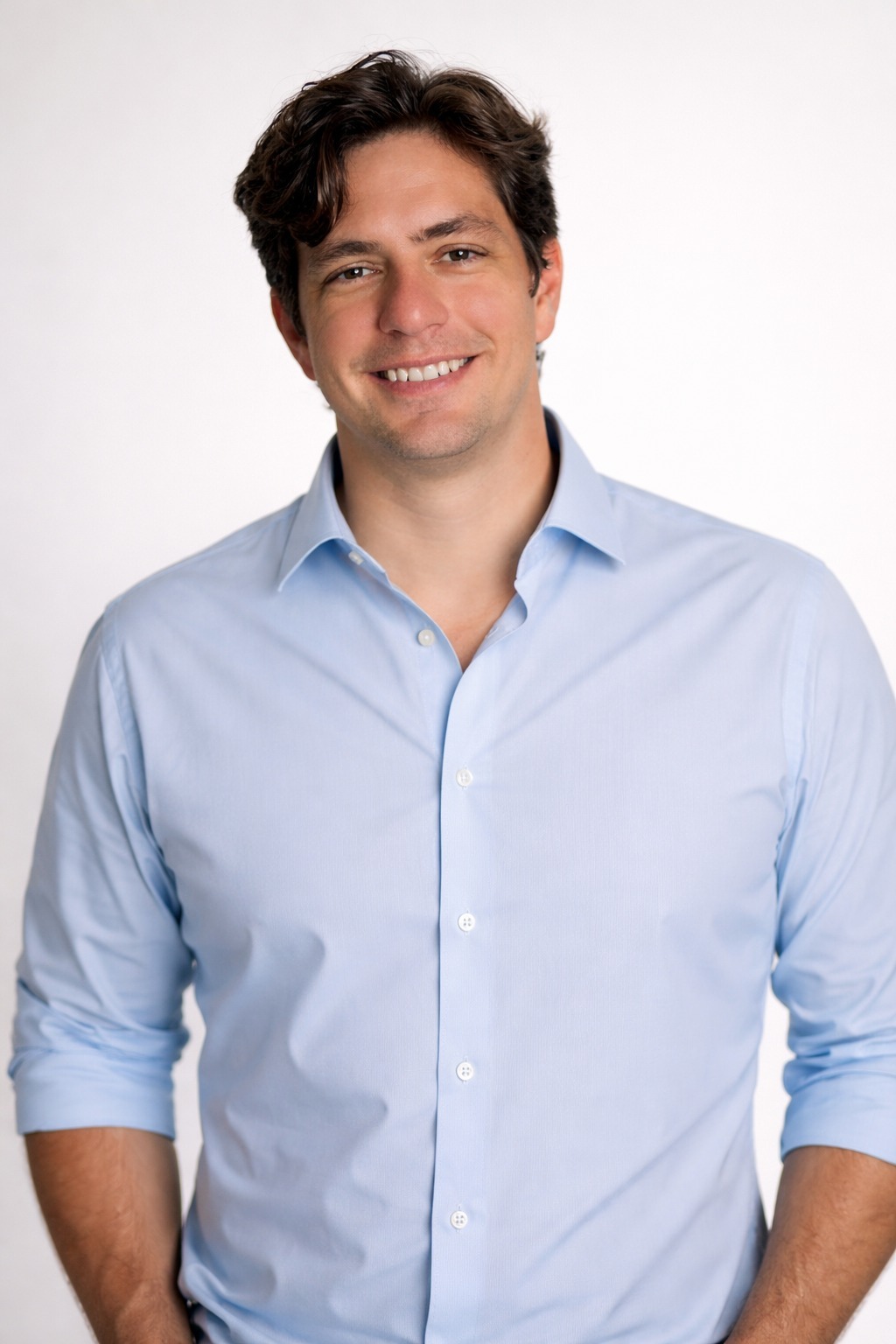 Paulo Jelihovschi de pé, sorri, usando camisa azul clara de manga comprida
