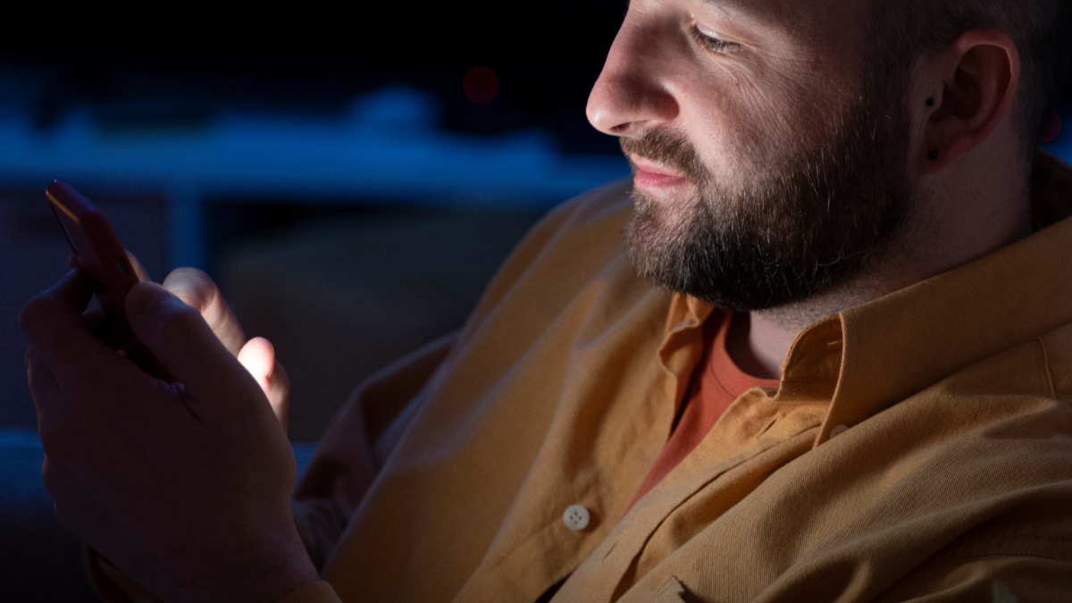 homem usando celular em um ambiente escuro, como cinema