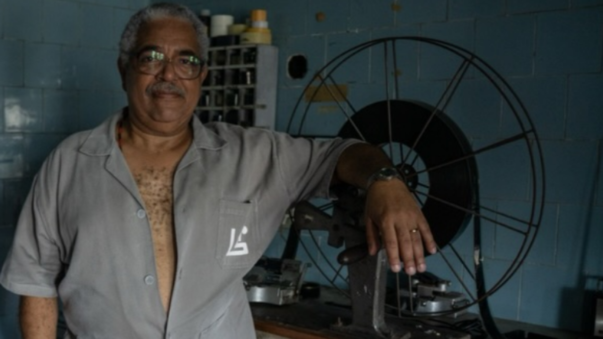 homem de camisa semiaberta em frente a projetor antigo de cinema