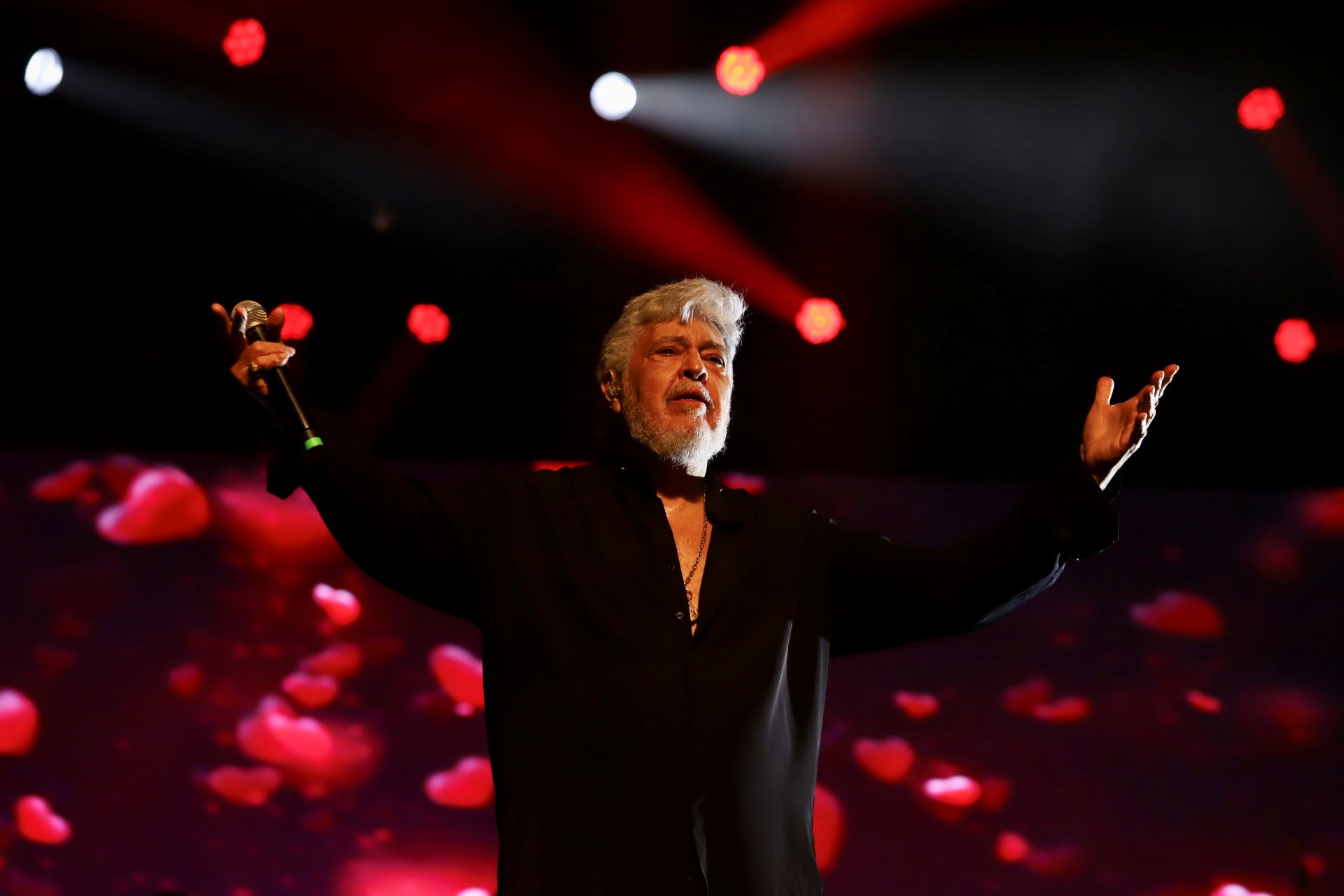 Sidney Magal veste roupa preta e está com os braços abertos em cima do palco
