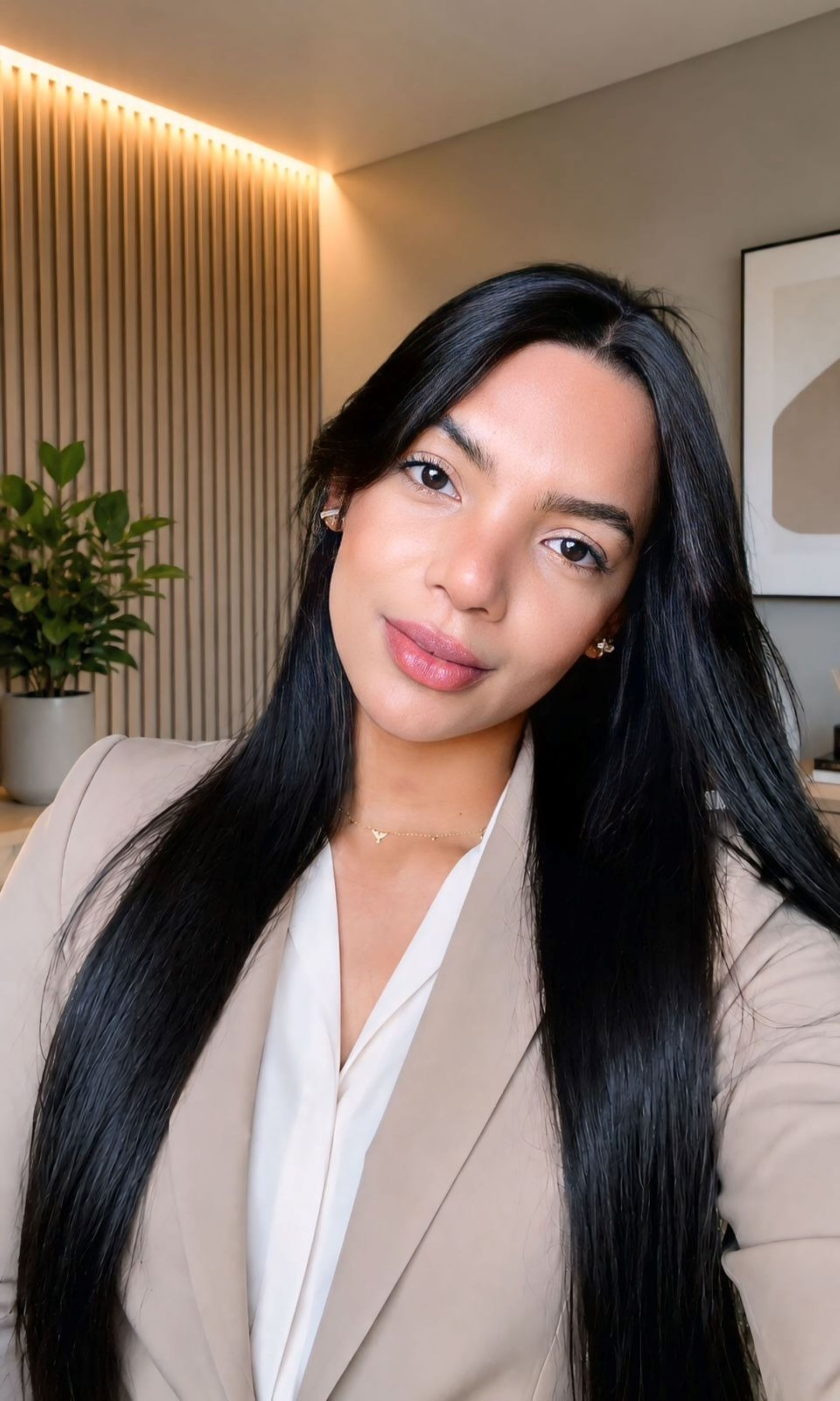 Com a cabeça pendendo para sua esquerda, Tayane Andrade tem cabelos pretos compridos e usa blazer de acinzentada
