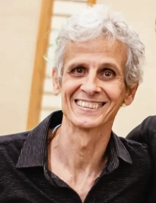 Carlos Rennó tem cabelos brancos e está sorrindo