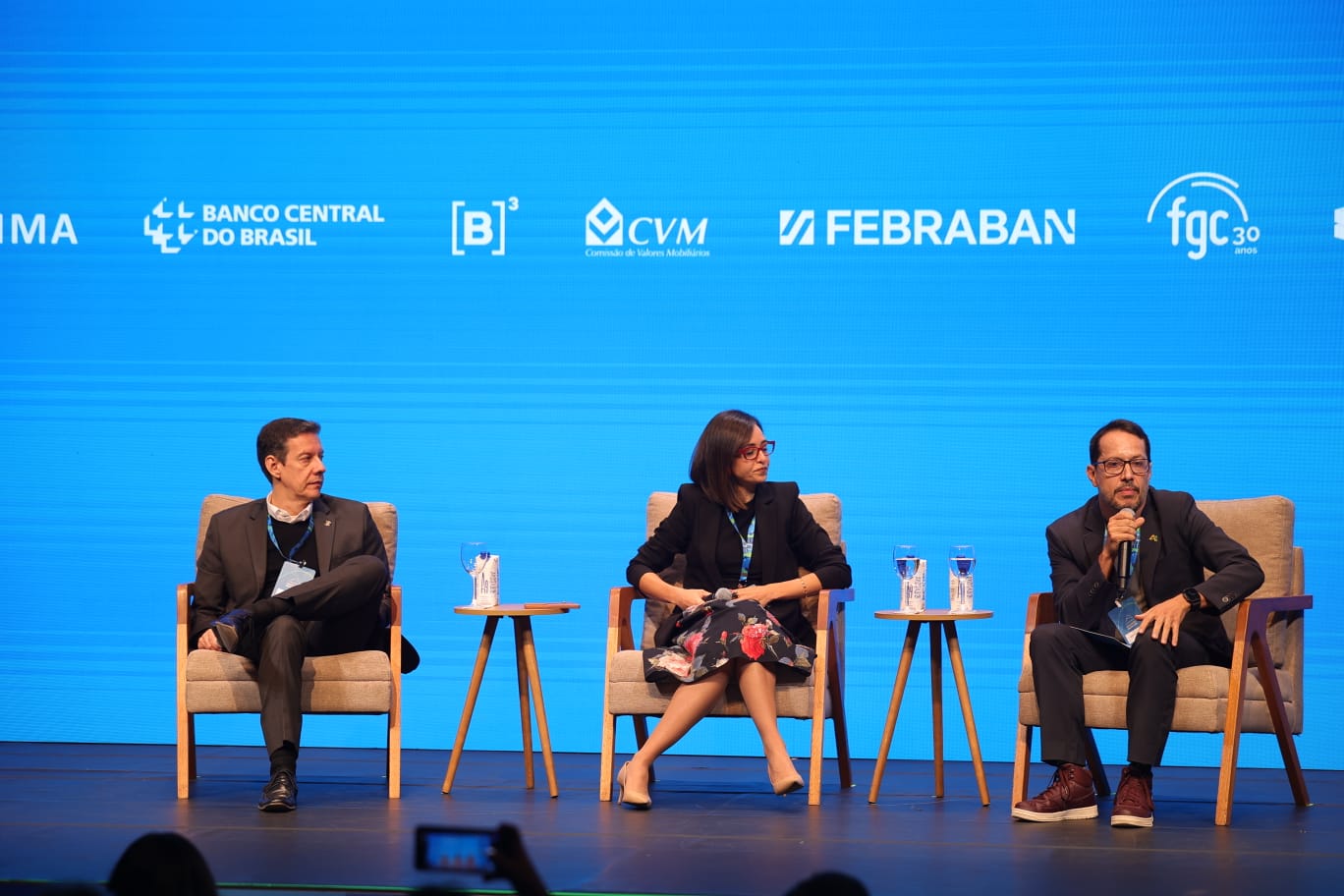 palco de evento obre educação financeira com três palestrantes