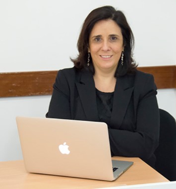 Frente a um notebook aberto sobre uma mesa, Elza Veloso sorri