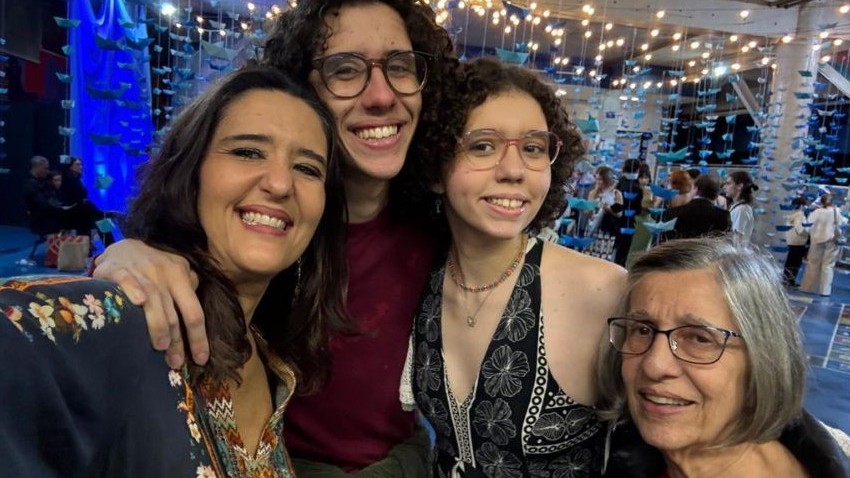 Maria Helena é uma mulher idosa e está ao lado da filha Cláudia e dos netos