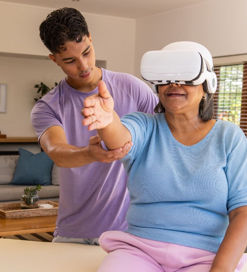 Idosa usa um headset de realidade virtual enquanto uma fisioterapeuta orienta os movimentos do braço