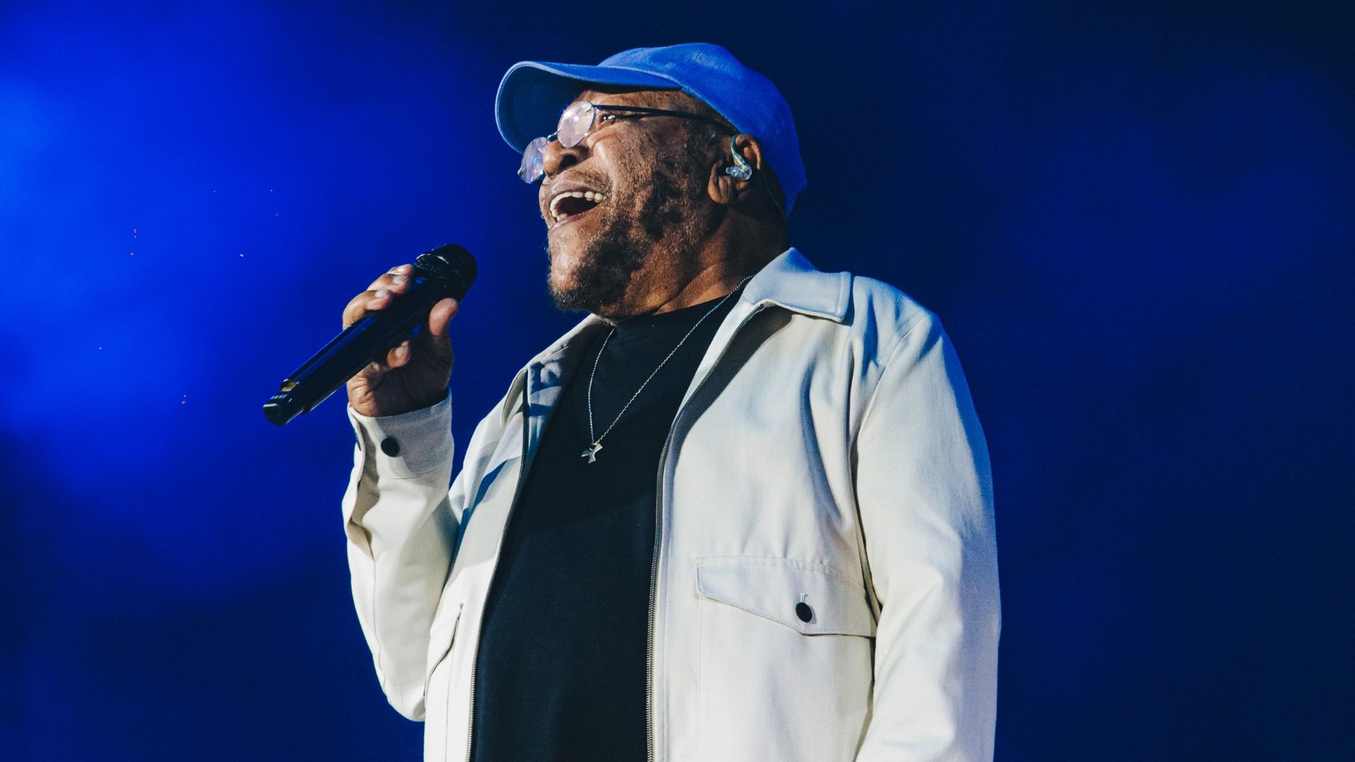 Martinho da Vila usa boné azul, camisa preta e jaqueta branca e segura microfone enquanto canta