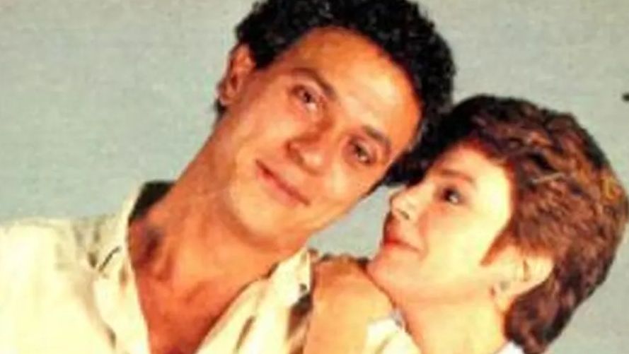 O ator está com cabeça inclinada e a encosta na atriz ao seu lado