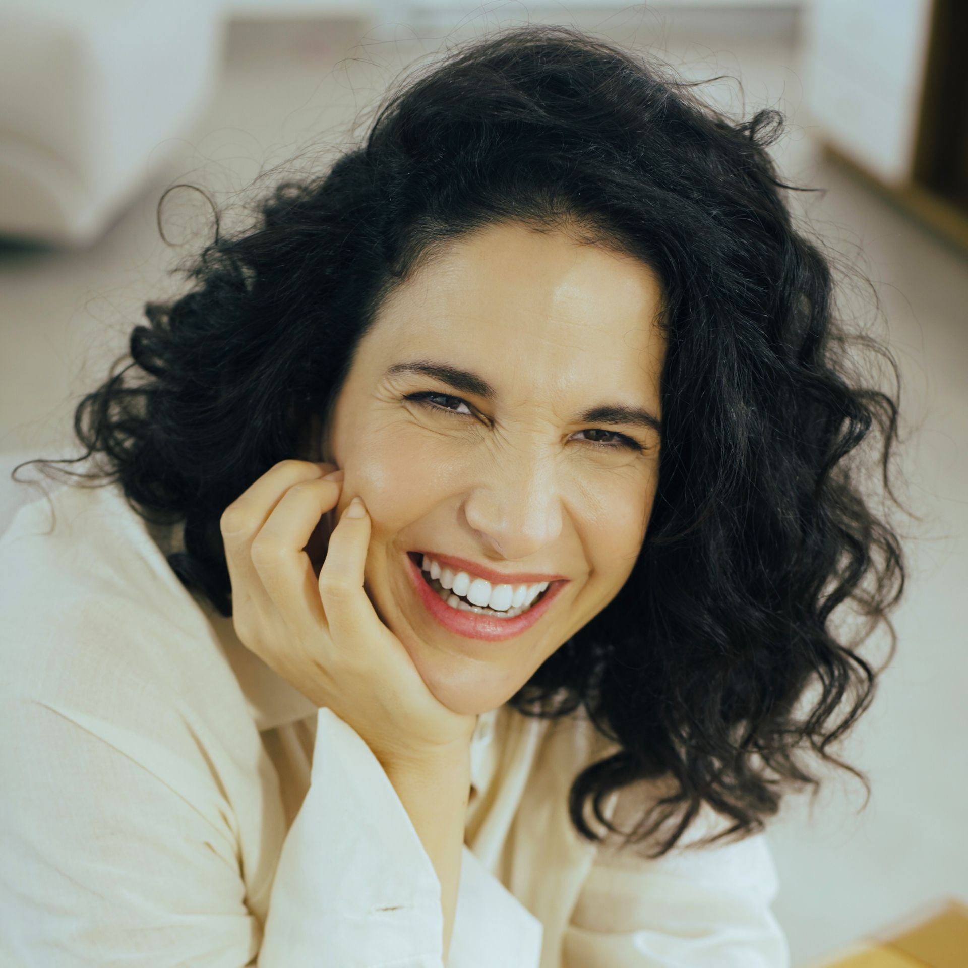 Verônica Ferriani está usando roupa branca, sorrindo e apoiando um dos lados do rosto na mão