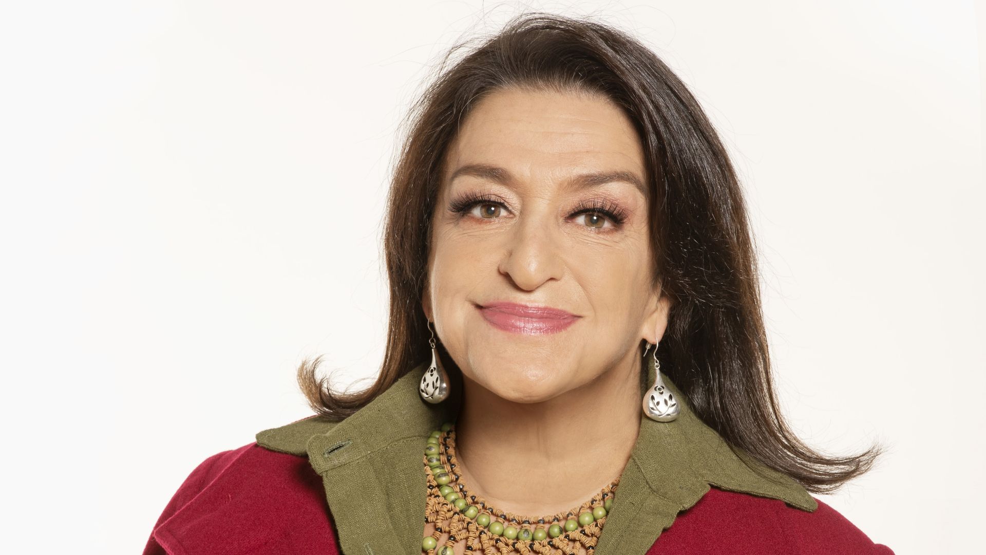 Grace Gianoukas tem cabelos lisos, brincos, colar e casaco vermelho com gola esverdeada