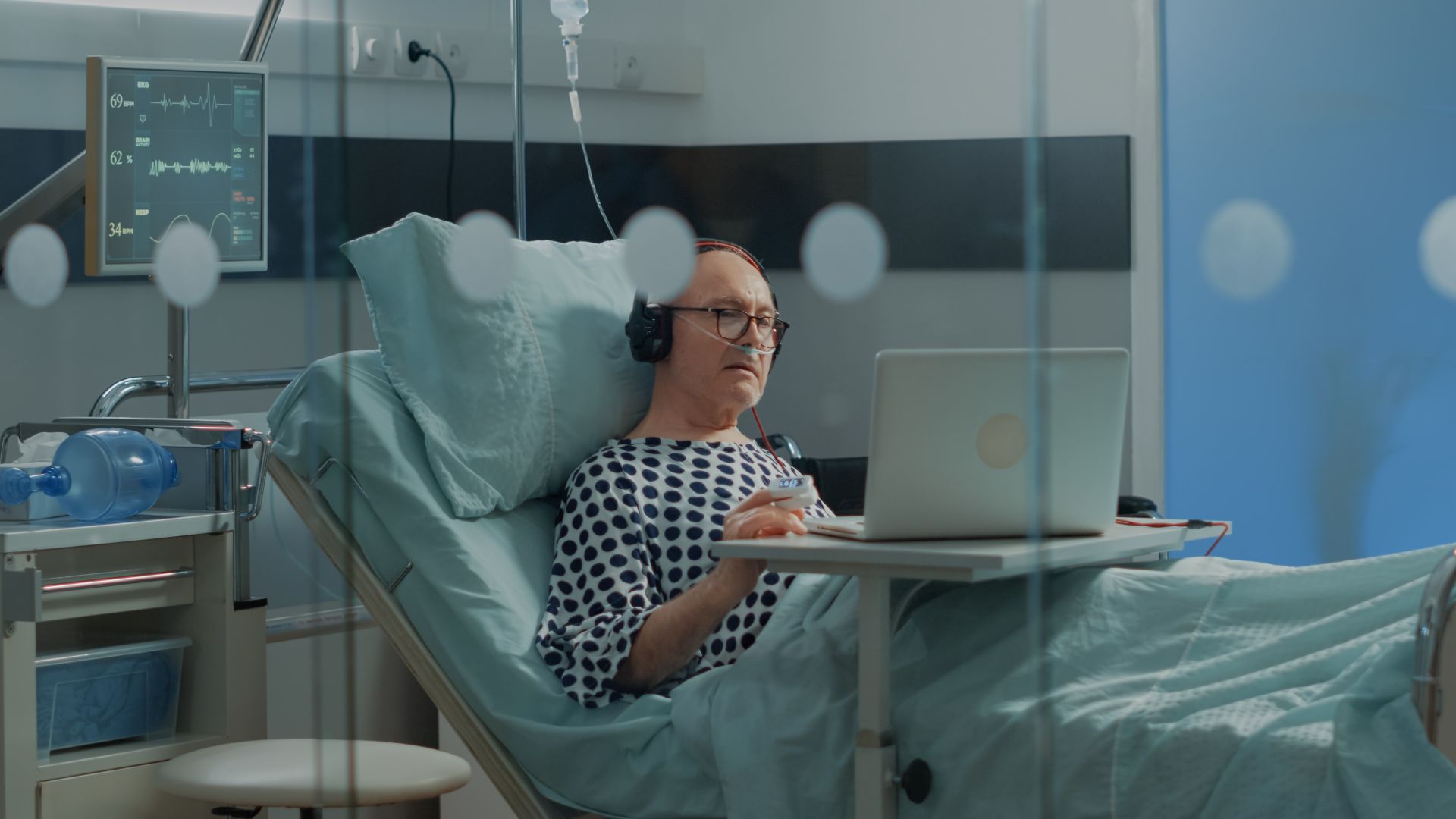 homem em uma cama de hospital com fones de ouvido e computador