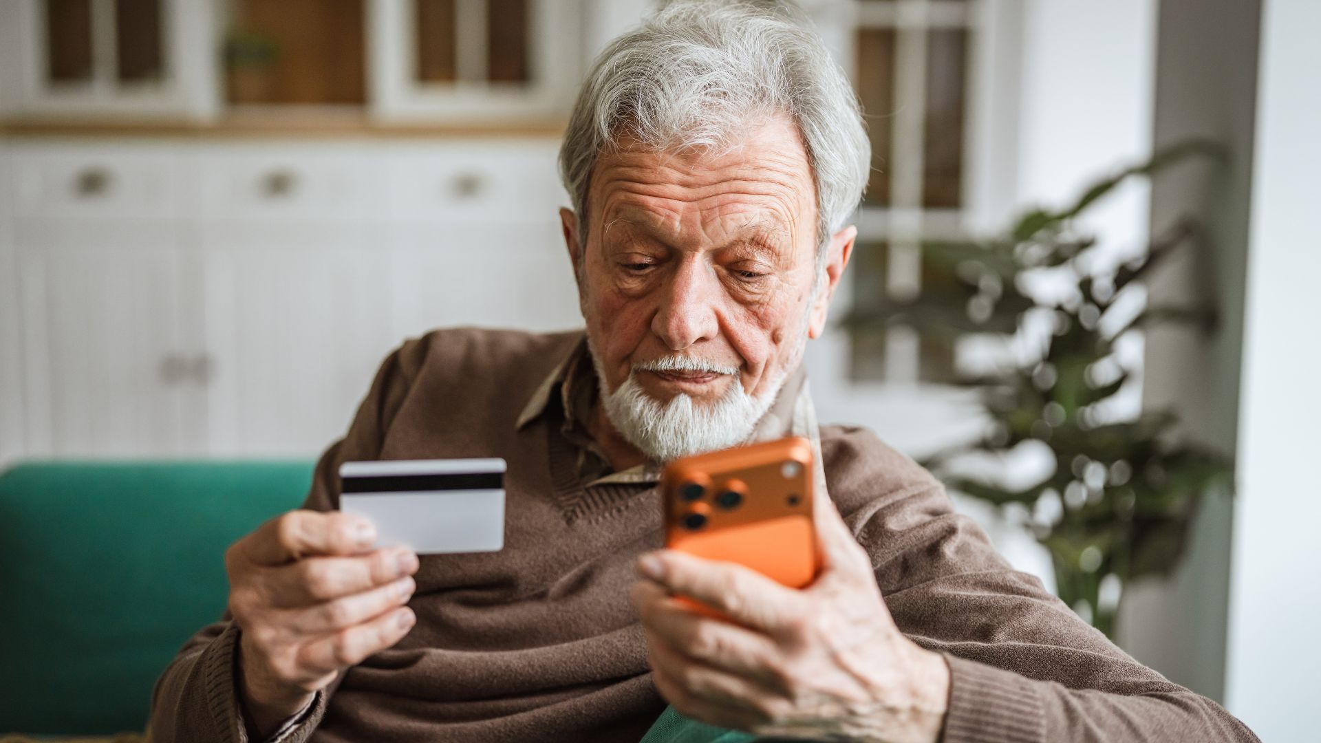 idoso realizando compra no celular e segurando um cartão