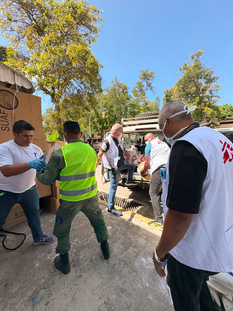 Profissionais de colete branco descarregam caixas de suprimentos de um veículo para as vítimas do terremoto.