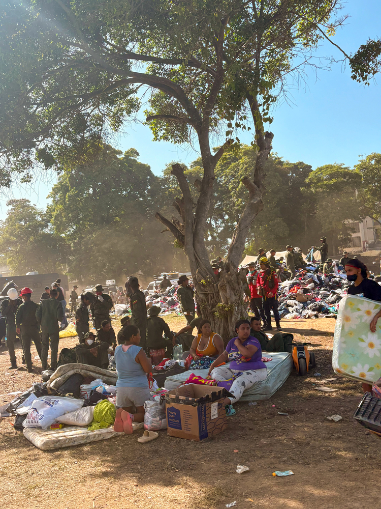 Desabrigados pelo terremoto na Venezuela sentam em colchões sob árvores enquanto equipes organizam doações ao fundo.