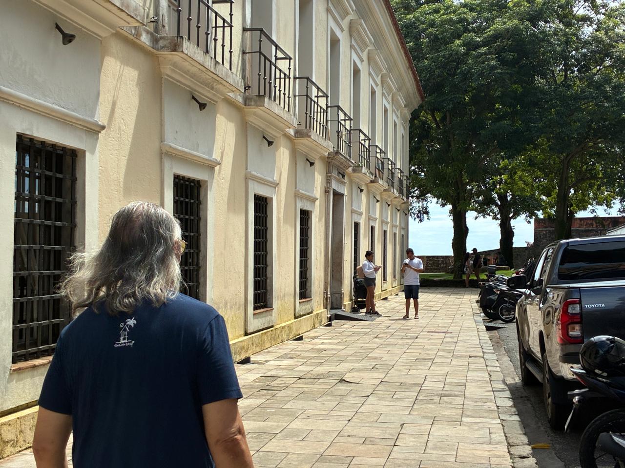 Cantor Nilson Chaves caminha de costas por calçada de pedras junto a casarão histórico em Belém.