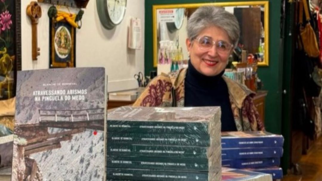 Usando óculos, Blanche de Bonneval sorri atrás de pilha de livros de sua autoria