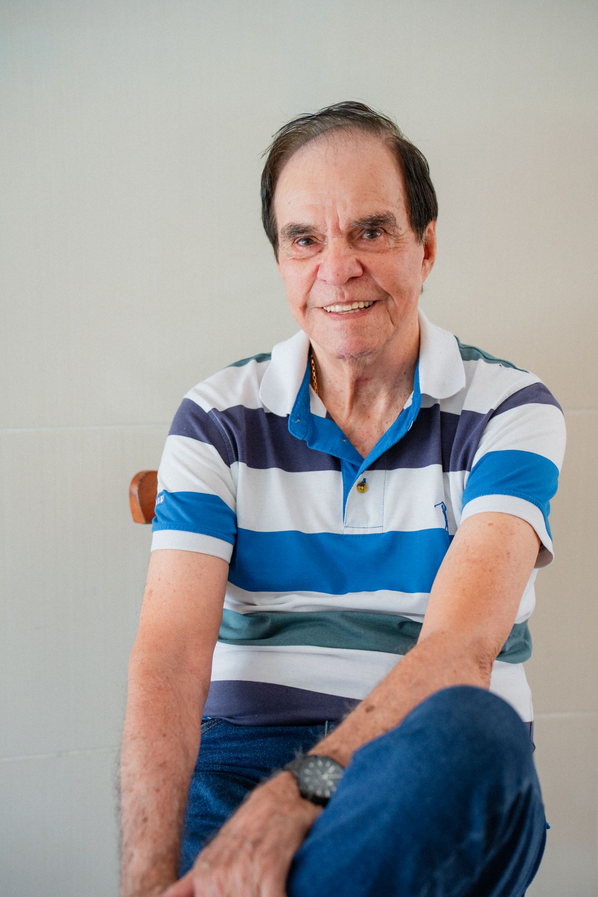 Almir Rangel posa para foto sentado de camisa listrada